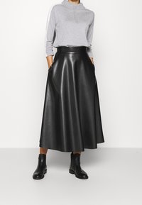 Zwarte leren maxi-rok met een hoge taille, voorzien van zijzakken en een gladde textuur, gecombineerd met een grijze longsleeve top en zwarte enkellaarzen.