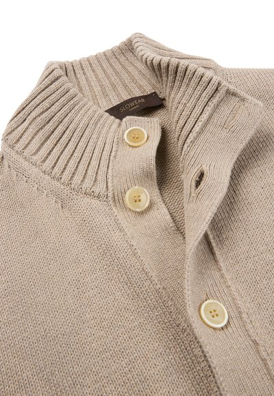 Cardigan beige lavorato a maglia con colletto a coste e tre bottoni color crema, che mostra parte della parte anteriore e dello scollo.
