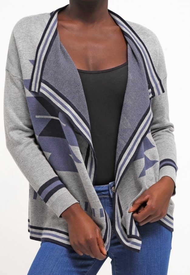 Personne portant un cardigan à motifs gris et bleu ouvert devant, un top noir et un jean bleu, ajustant le cardigan à la taille.