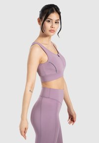 Sujetaemonos deportivos morados con un escote redondeado y tirantes gruesos, que incluye un bolsillo con cremallera. Combinado con leggings morados de cintura alta, de textura suave.