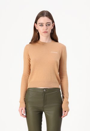 Beige kasjmir genser med rund hals, ribbede mansjetter og kant. Har en liten hvit logo på brystet. Kombinert med mørkegrønne bukser.