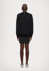 Un pull en tricot noir avec des pois blancs, des poignets et un ourlet côtelés. Associé à une jupe assortie. Des chaussures argentées métalliques complètent le look.