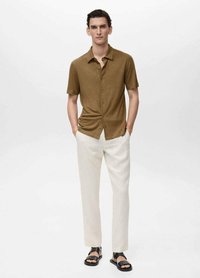 Camicetta marrone a maniche corte con bottoni e motivo texture, abbinata a pantaloni beige a sigaretta e sandali neri.