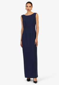 Navyblauwe, mouwloze maxi-jurk met een bootnekontwerp, voorzien van subtiele plooien en een recht silhouet, gecombineerd met zwarte hakken.