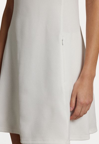 Balta A līnijas kleita ar teksturētu audumu, kurai ir sānu rāvējslēdzis. Apakšgala forma ir izvērsta, un dizains ir vienkāršs un minimālistisks.