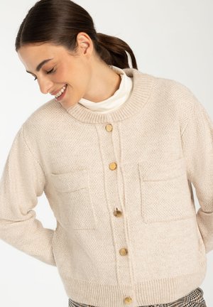 Beige knitted cardigan with a round neck, two front pockets, and gold buttons. Textured fabric and ribbed hem detail.