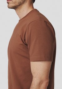 Brązowa bawełniana koszulka z krótkim rękawem, okrągłym dekoltem i minimalistycznym wzorem. Gładka faktura i prosty krój.