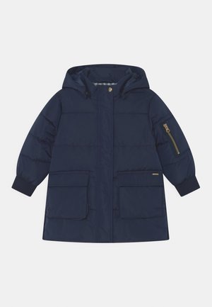 Manteau matelassé à capuche bleu marine avec fermeture à pressions et zip devant, deux grandes poches à rabat, poignets côtelés et poche zippée sur la manche.