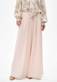 Wijde pantalon in zachtroze stof met een gladde textuur, met een hoge taille en een vloeiende silhoeët. Draag het met een bloes met bloemen.