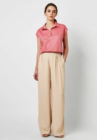 Helle rosa Bluse mit kurzen Ärmeln und Kragen, kombiniert mit hoch taillierten beigen weiten Hosen aus glattem Material mit subtiler Textur.