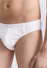 Witte katoenen slip met elastische tailleband en een klein label. Glad textuur en aansluitend ontwerp. Zichtbare huidtinten eromheen.