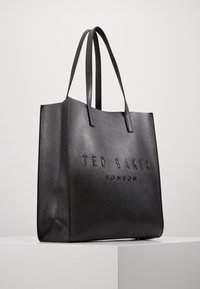 Sac cabas noir en matière texturée, avec logo embossé "TED BAKER LONDON", double poignée et forme structurée.
