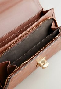 Portefeuille en cuir marron avec zip et fermoir dorés, comportant plusieurs fentes pour cartes et un intérieur en tissu lisse. Extérieur texturé et détails de couture.