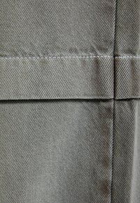 Närbild av grått twilltyg med synlig sömnad och vikta sömmar som bildar horisontella och vertikala linjer.