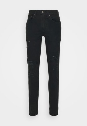 Jean slim noir avec des déchirures usées sur l'avant des cuisses et des genoux, style cinq poches, fermeture par bouton et fermeture éclair.