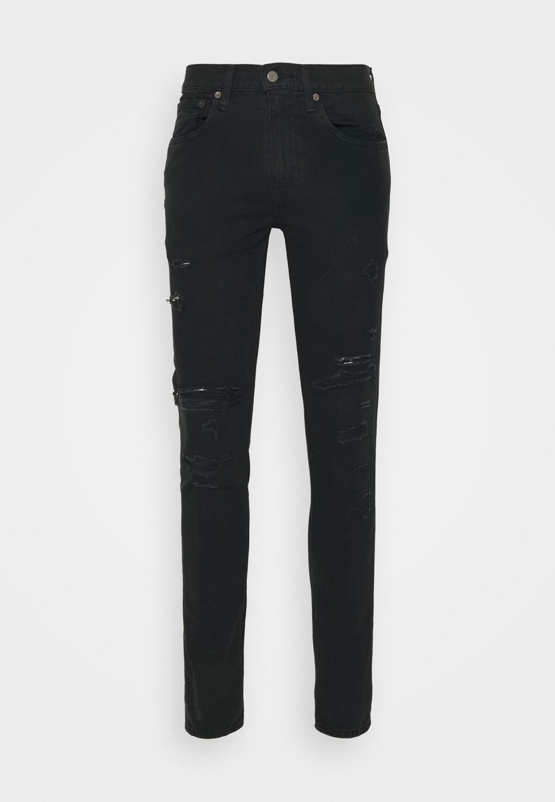 Jean slim noir avec des déchirures usées sur l'avant des cuisses et des genoux, style cinq poches, fermeture par bouton et fermeture éclair.