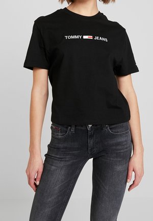 Černé bavlněné tričko s bílým logem "TOMMY JEANS". Krátké rukávy, kulatý výstřih, mírně zkrácený střih. Spárováno s tmavě šedými džíny.