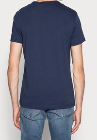 Marinblå bomullströja med kort ärm, rund halsringning och en enkel baksidesdesign, stoppad i ljusblå jeans.