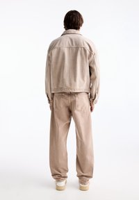 Chaqueta y pantalones de denim beige, corte relajado, textura suave, costuras visibles, con puños elásticos, combinados con zapatillas blancas.
