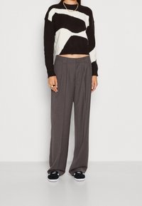 Svart och vit, kortad tröja med vågig mönster, tillsammans med grå vida byxor och svarta sneakers med vita sulor.