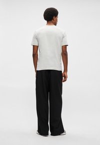 Svetlo šedé tričko s krátkym rukávom so simple dizajnom, skombinované s voľnými čiernymi nohavicami. Hladká textura, žiadne viditeľné vzory alebo akcenty.