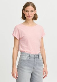T-shirt rosa a maniche corte con scollatura rotonda, dalla consistenza morbida e con i risvolti, abbinato a jeans grigi chiari a vita alta.