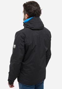 Schwarze wasserdichte Jacke mit Kapuze, mit einer blauen Innenauskleidung und einem Logo auf dem linken Arm. Glatte Textur und taillierte Passform.