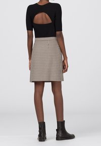 Černý žebrovaný top s výstřihem na zádech, spárovaný s béžovou a černou sukní v kostkovaném vzoru. Modelka má na sobě černé kotníkové boty.