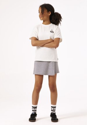 Camiseta de algodón blanca con un diseño de cereza negra, combinada con una falda de cuadro gris. Medias negras con rayas blancas y zapatillas negras completan el conjunto.