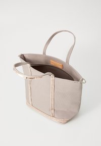 Beige tyghandväska med en strukturerad form, med metallisk roséguld detaljer längs kanterna och ett dragkedjefack inuti.