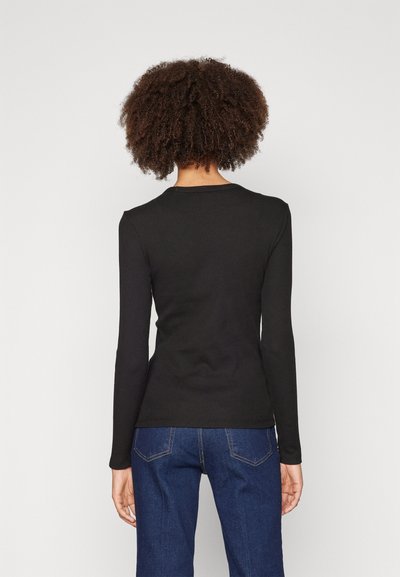 Haut noir à manches longues avec une texture côtelée et un col rond, associé à un jean en denim bleu avec un design simple de poche arrière.