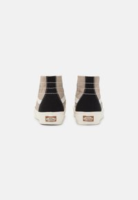 Höga sneakers i beige och svart canvas med vit söm, med en krämfärgad gummisula och ikonisk logotyp på hälen.
