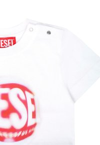 Biała koszulka z dużym czerwonym logo "DIESEL", krótki rękaw i srebrny nap na ramieniu. Miękka bawełniana tkanina.