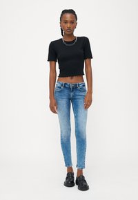 Melnas ribota īsām piedurknēm crop top krekls, kas sader ar ziliem šauriem džinsiem. Džinsiem ir izbalējusi krāsa un redzamas šuvju detaļas. Melni loafers.