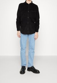 Musta samettikankainen nappipaita, jossa rintatasku, yhdistetty vaaleansinisiin farkkuihin ja mustiin nauhallisiin kenkiin. Sileä pinta, rento istuvuus.