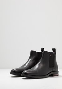 Botas de cuero negro hasta el tobillo con paneles elásticos en los lados, punta redonda, tacón bajo en bloque y acentos en rojo y negro contrastantes en el tacón.