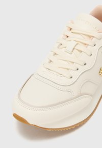 Lys kremfargede sneakers med glatt syntetisk lær, rund tå, beige snøringer, diskrete sømdetaljer og en teksturert gummisåle.