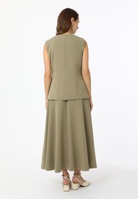 Haut sans manches vert olive associé à une jupe longue assortie. Tissu lisse, coutures discrètes et détails au dos. Chaussures à talons carrés visibles.