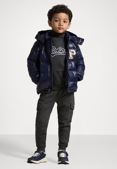 Ναυτικό μπουφάν με κουκούλα, γκρι φούτερ με λογότυπο, σκούρο γκρι cargo παντελόνι και ναυτικές αθλητικές πατούσες με λευκές λεπτομέρειες.