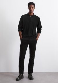 Black long-sleeve polo with a zip collar, paired with dark pants and black lace-up shoes. Smooth fabric with a slim fit design.