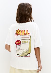 Witte katoenen t-shirt met een grafisch ontwerp van een afhaalzak met dumplings, rood en gele tekst, en voedingsinformatie. Korte mouwen.
