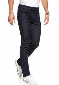 Ciemnoniebieskie dżinsy o dopasowanym kroju, z klasycznym pięciopocketowym designem i subtelnymi detalami przeszycia. Noszone z białymi sneakersami.