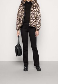 Chaqueta acolchada en beige y estampado de leopardo marrón; cierre con cremallera en la parte delantera, capucha, puños elásticos. Top negro, vaqueros acampanados, y zapatillas negras con un bolso.