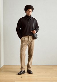 Camisa negra de cuello con mangas largas, pantalones de pana beige, botas marrón oscuro y un pequeño bolso cruzado negro. Texturas suaves, corte relajado.