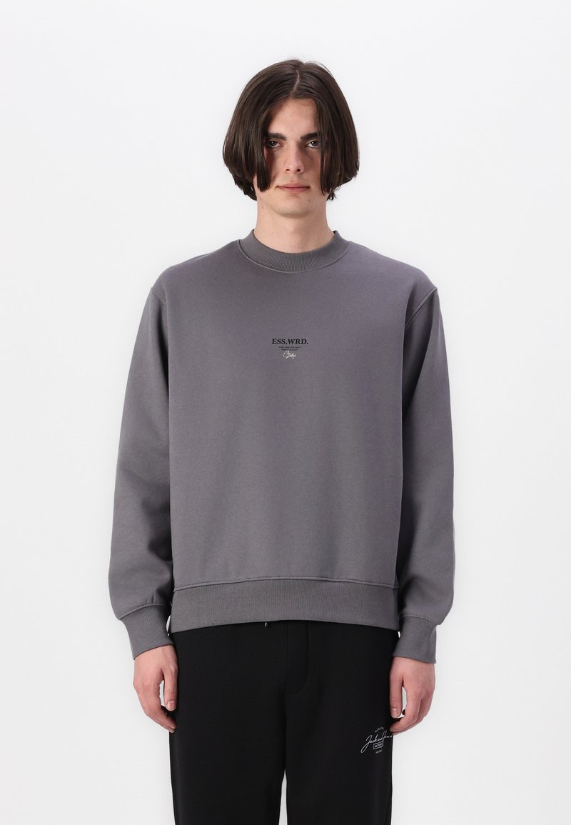 Grå sweatshirt med ribbede rund hals og manchetter. Har sort "ESS.WRD." tekst på brystet. Kombineret med sorte bukser for et komplet outfit.