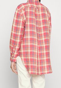 Červená a žlutá kostkovaná košile s dlouhými rukávy, knoflíkovými manžetami a zadním skladem, vyrobena z lehkého materiálu. Zaoblený lem s postranními rozparky.