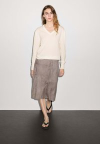 Maglione a maglia beige chiaro con scollo a V, abbinato a una gonna in suede grigia con dettaglio a cordoncino e sandali neri infradito.