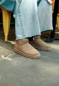 Bottes de cheville en daim beige au design simple avec semelles en caoutchouc, assorties à un jean en denim clair délavé, couvrant partiellement les bottes.