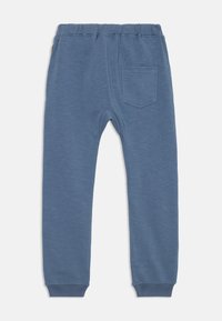 Blaue Jogginghose mit elastischem Bund, einem einzelnen Gesäßtasche und gerippten Knöcheln, flach auf einem weißen Hintergrund ausgelegt.