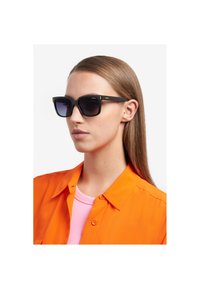 Ochelari de soare cu ramă din plastic negru și lentile întunecate. Designul este de formă pătrată, având accente aurii subtile și branding pe brațe.